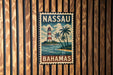 A vintage-style metal sign with the text "NASSAU BAHAMAS" and an illustration of a lighthouse and palm trees, mounted on a wooden wall.
