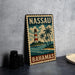 A vintage-style metal sign with a lighthouse and palm trees, depicting the Bahamas, is displayed on a table.