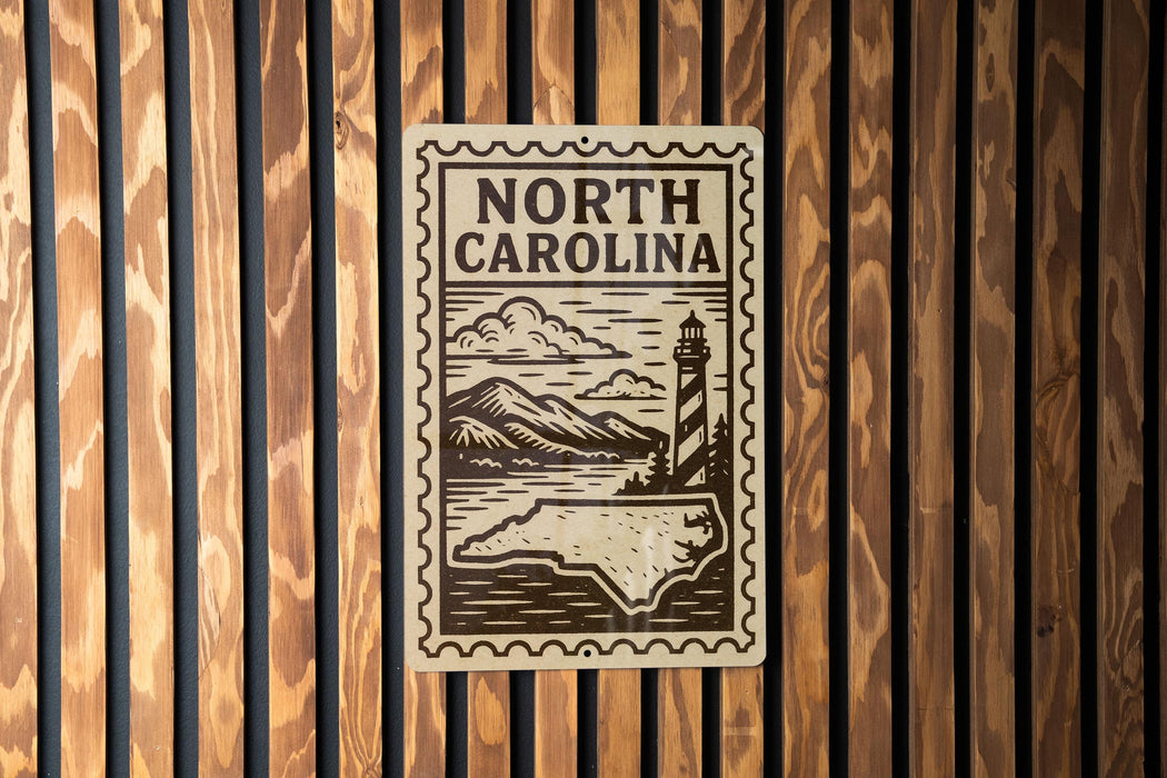 A metal sign with the text "NORTH CAROLINA" and an illustration of a lighthouse and mountains, mounted on a wooden wall.