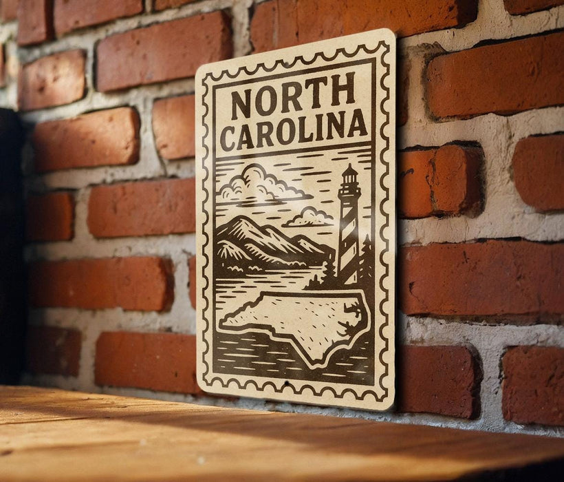 A decorative metal sign with the text "NORTH CAROLINA" and an illustration of a lighthouse and mountains, mounted on a brick wall.
