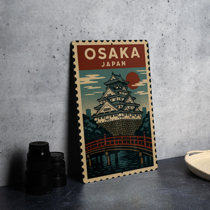 A vintage-style poster of Osaka, Japan, featuring a castle-like structure and a bridge, is displayed on a gray wall.