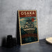 A vintage-style poster of Osaka, Japan, featuring a castle-like structure and a bridge, is displayed on a gray wall.