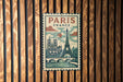 A vintage-style poster of Paris, France, featuring the Eiffel Tower and other iconic landmarks, is displayed on a wooden wall.