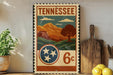 A vintage-style metal sign with the text "TENNESSEE" and a landscape illustration, featuring mountains, trees, and a pine tree.