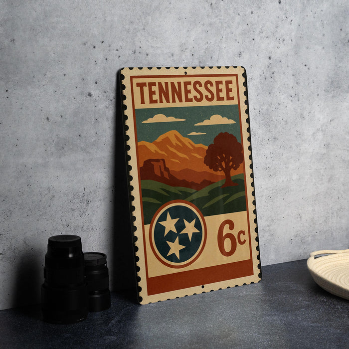 A vintage-style metal stamp from Tennessee featuring a landscape scene with mountains, trees, and a tree with three stars.
