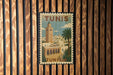 A vintage-style postage stamp from Tunisia featuring a cityscape with a tall tower and palm trees.