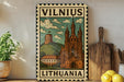 A vintage-style metal sign depicting a castle and a hill, with the text "Vilnius Lithuania" on it, is displayed on a shelf next to a wooden cutting board and a potted plant.