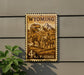 A vintage Wyoming postage stamp featuring a dinosaur and a cowboy on horseback, mounted on a wall.