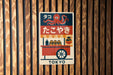 A colorful poster with an illustration of an orange and black octopus, along with Japanese text and a wheeled cart, mounted on a wooden wall.