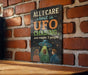 a sign with the text "All I care about is UFO chasing... and maybe 3 people" against a brick wall background.