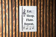 a sign with the text "Eat. Sleep. Flute. Repeat." and a musical note symbol, placed on a wooden wall.