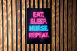 a sign with the text "EAT. SLEEP. NURSE. REPEAT." in neon colors, mounted on a wooden wall.