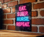 A neon sign with the text "EAT. SLEEP. NURSE. REPEAT." displayed on a brick wall.