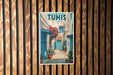 A vintage-style poster of a narrow street in Tunisia, featuring colorful buildings, flowers, and a blue door.