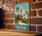 A vintage-style metal sign with a tropical scene of a house and palm trees, mounted on a brick wall.