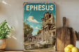 A vintage-style metal sign with the word "EPHESUS" displayed prominently, featuring an illustration of an ancient Greek temple or ruins against a blue sky with a full moon.