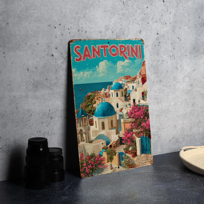 A vintage-style metal sign with the word "SANTORINI" prominently displayed, depicting a picturesque coastal town with colorful buildings, blue domes, and a clear blue sky.