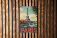A vintage-style metal sign depicting the Eiffel Tower in Paris, France, is displayed on a wooden wall.