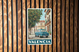 A vintage-style poster of a car parked on a street in a Spanish town, with a tree and buildings in the background.
