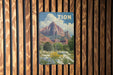 A vintage-style poster of a mountainous landscape with a large red rock formation and a blue sky with clouds, hanging on a wooden wall.