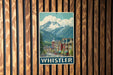 A vintage-style poster of Whistler, a mountain town in British Columbia, Canada, is displayed on a wooden wall.