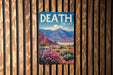 A vintage-style metal sign with the text "DEATH VALLEY" is displayed on a wooden wall, featuring a scenic mountain landscape with colorful flowers.