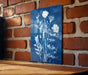 A blue sign with white floral designs is mounted on a brick wall.