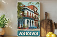 A vintage-style metal sign displaying a colorful image of a building with a blue car parked in front, surrounded by lush greenery.