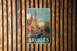A vintage-style metal sign with a painting of a cityscape and a tower, mounted on a wooden wall.