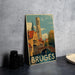 A vintage-style metal sign displaying the image of the city of Bruges, Belgium, with a church tower and a bridge in the background.