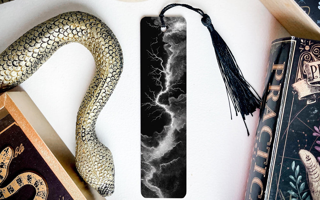 a black and white bookmark with a lightning bolt design, accompanied by a black tassel, and a book titled "Practice" on a white surface.