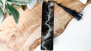 A black and white bookmark with a tassel attached, resting on a wooden surface.