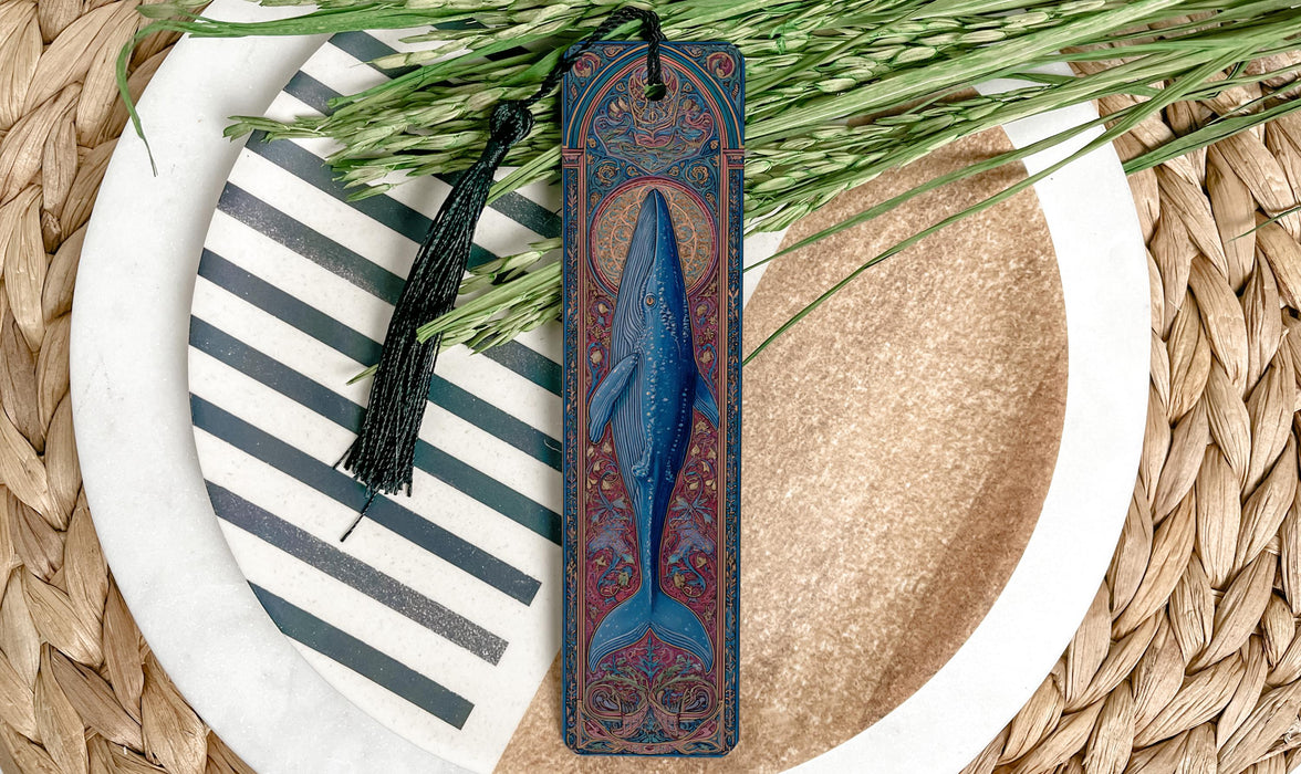 A decorative bookmark featuring a blue whale design rests on a plate with a striped pattern, surrounded by green foliage.