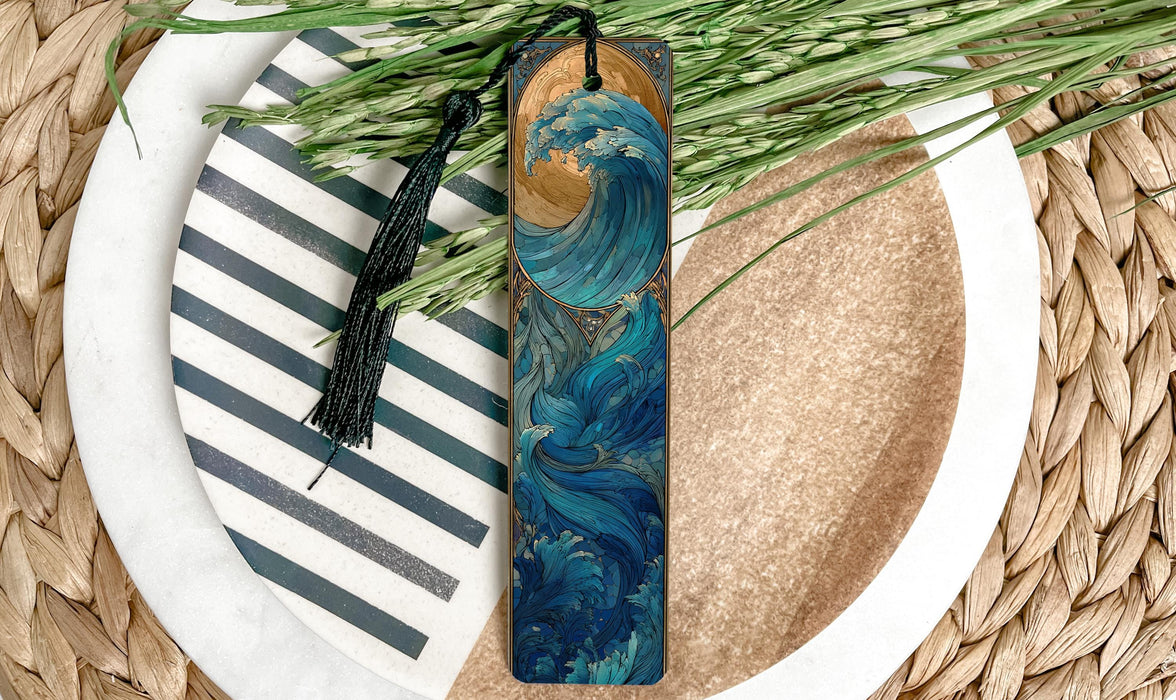 A wooden bookmark with a wave design and a black tassel is placed on a plate with a striped pattern and some green foliage.
