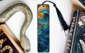 a decorative snake-shaped bookmark with a wave design on it, placed next to a book and a tassel.