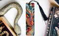 a dragon-themed bookmark with a black tassel, placed next to a book and a decorative snake-shaped object.