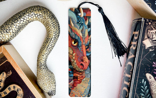 a dragon-themed bookmark with a black tassel, placed next to a book and a decorative snake-shaped object.