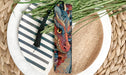 A colorful dragon-themed bookmark is placed on a plate with a striped pattern, surrounded by green grass.