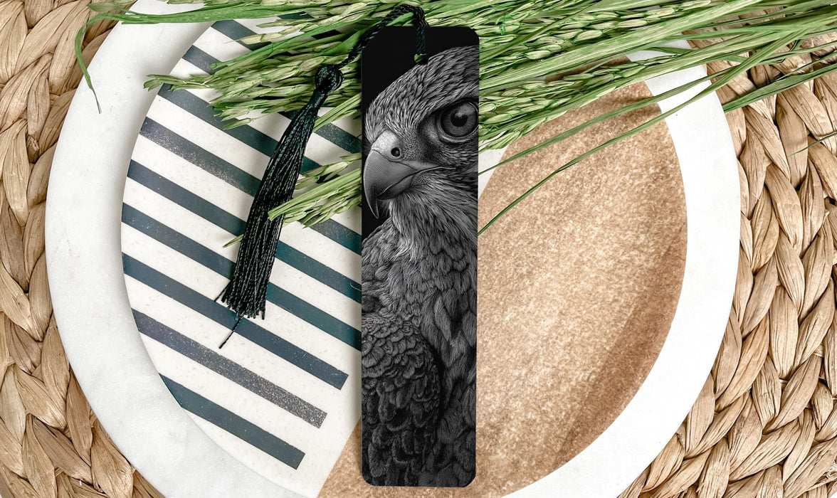 A close-up image of a black and white photograph of a bird of prey, likely a hawk, with a tassel hanging from its neck. The bird is positioned on a white plate with a black and white striped pattern, and there is a pile of green grass or leaves nearby.