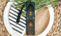 A decorative bookmark with an intricate design, placed on a plate with a striped pattern and a sprig of greenery.
