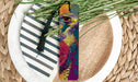 A colorful bookmark featuring a close-up of a bird's face is placed on a plate with a black tassel.