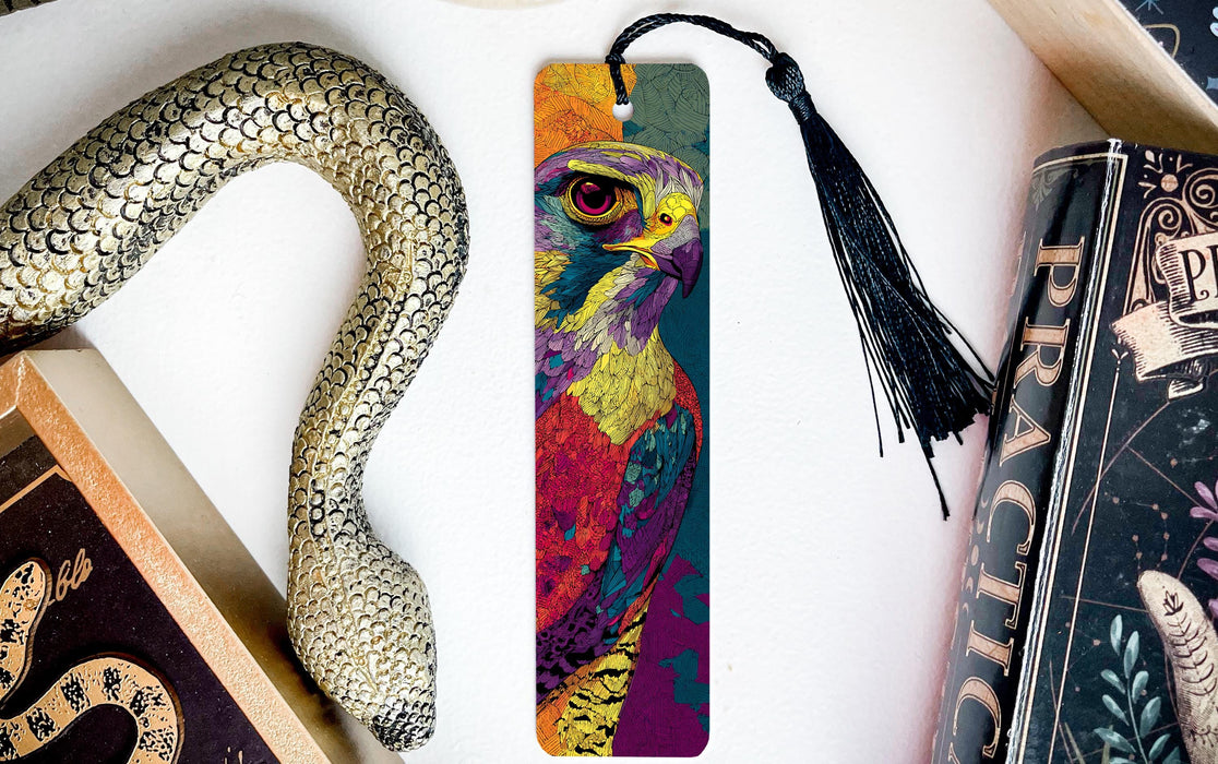 A colorful bird-like bookmark with a black tassel is placed on a white surface next to a book and a decorative snake.