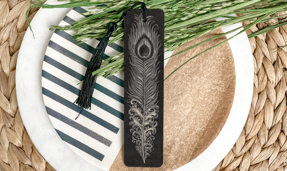 A decorative black bookmark with a feather design rests on a plate with a striped pattern, surrounded by green foliage.