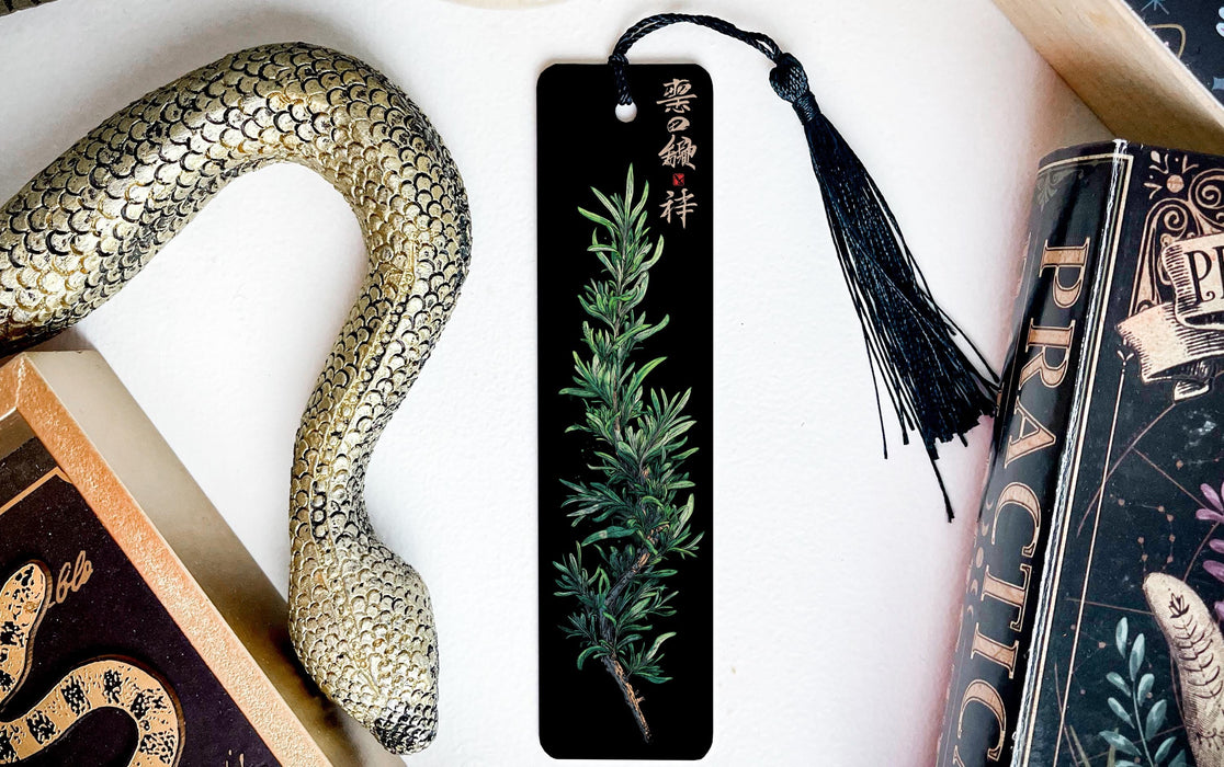 a black bookmark with a decorative snake design on it, placed next to a book and a decorative snake toy.