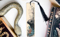 a decorative snake-shaped bookmark with a floral design, placed next to a book titled "Practice" and a black tassel.
