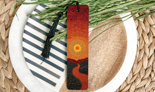 A decorative bookmark with a sun-like design is placed on a plate with a striped pattern, surrounded by green foliage.