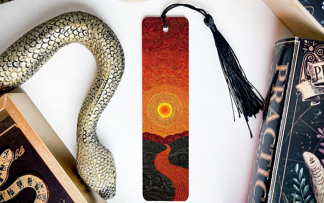 a snake-shaped bookmark with a sunset design, placed on a white surface next to a book and a decorative item.