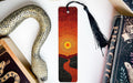 a snake-shaped bookmark with a sunset design, placed on a white surface next to a book and a decorative item.