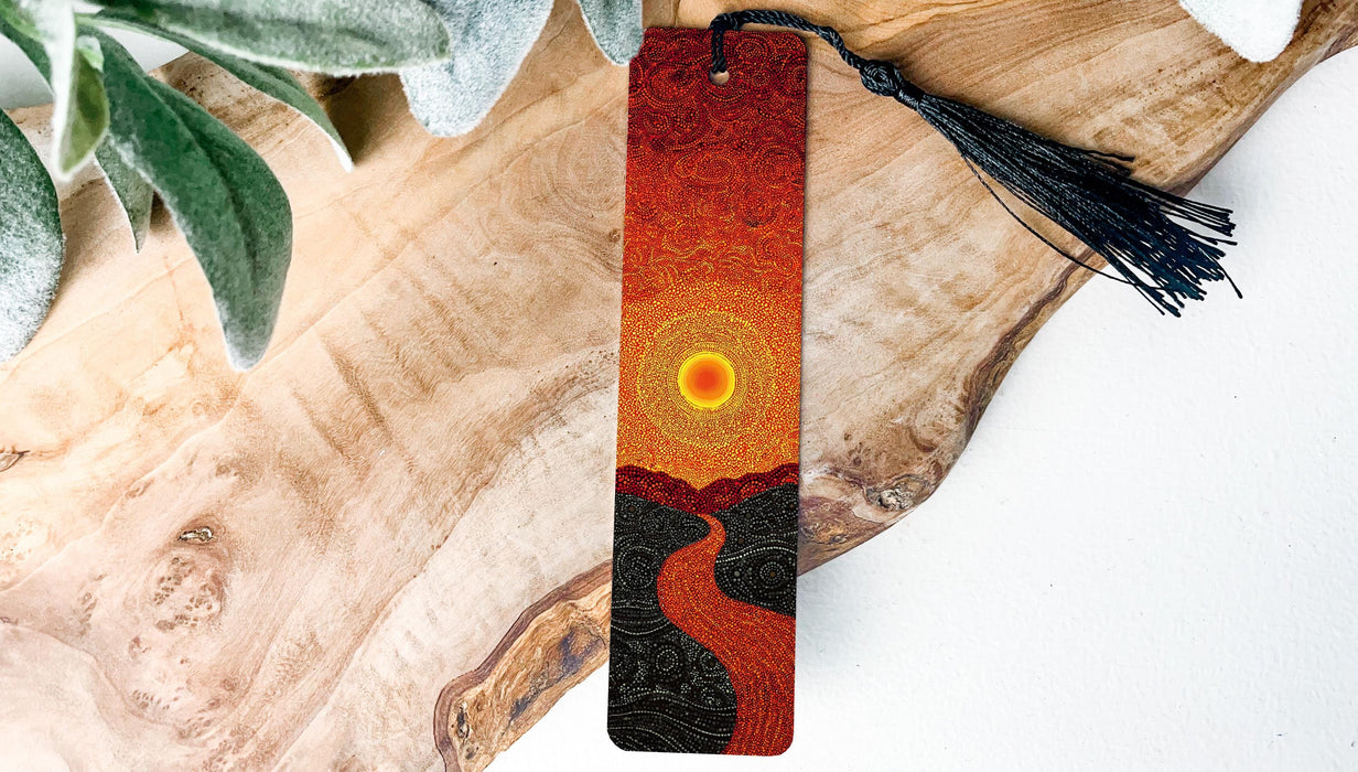 A wooden surface with a decorative bookmark featuring an abstract design of a sun and a winding path.