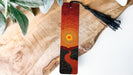 A wooden surface with a decorative bookmark featuring an abstract design of a sun and a winding path.